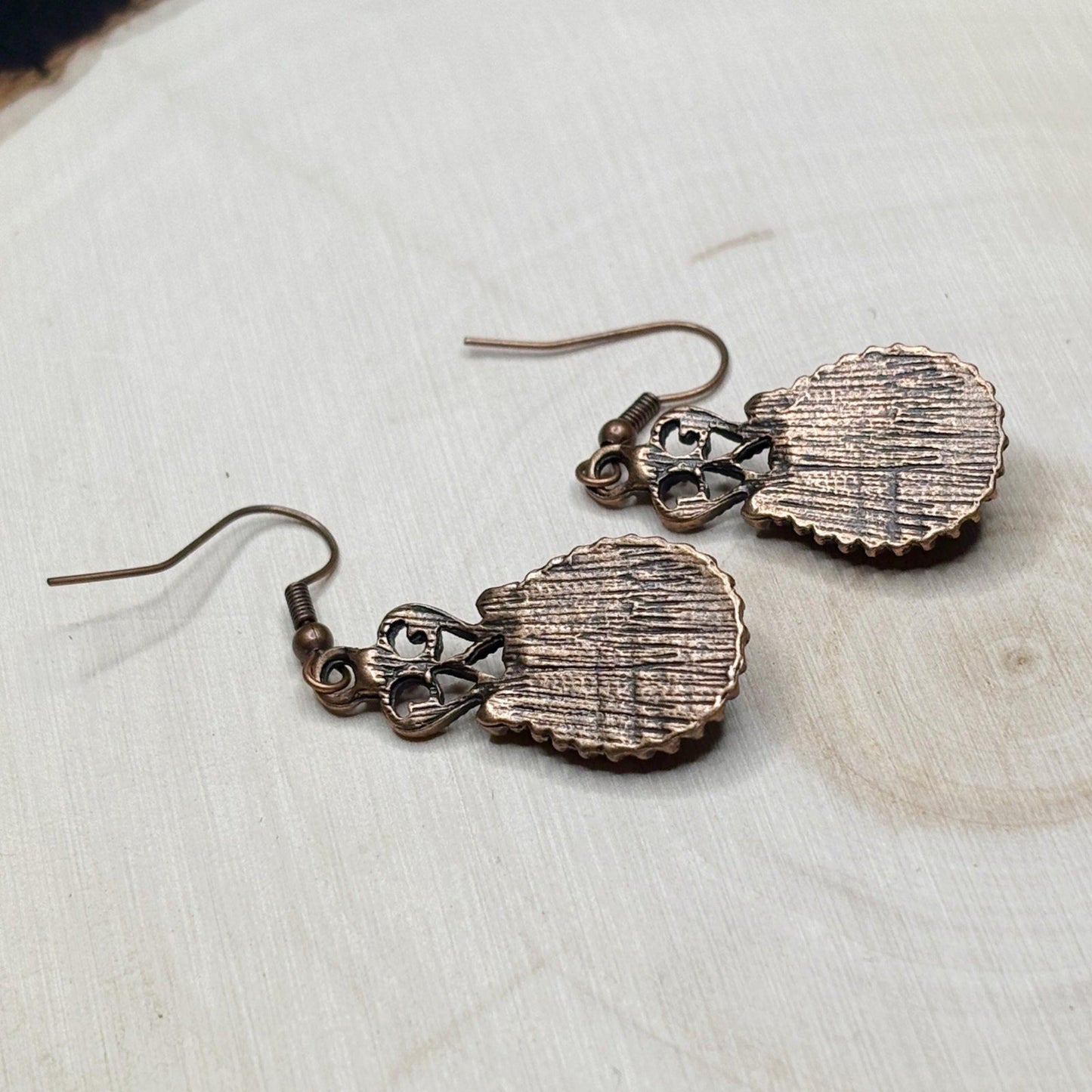 Pair of copper shell-shaped earrings on a light wooden surface