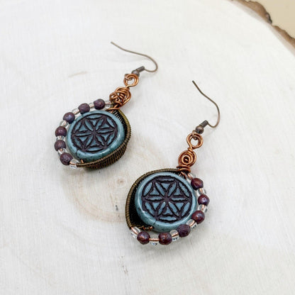 Pair of earrings with blue circular designs and purple beads on a white surface