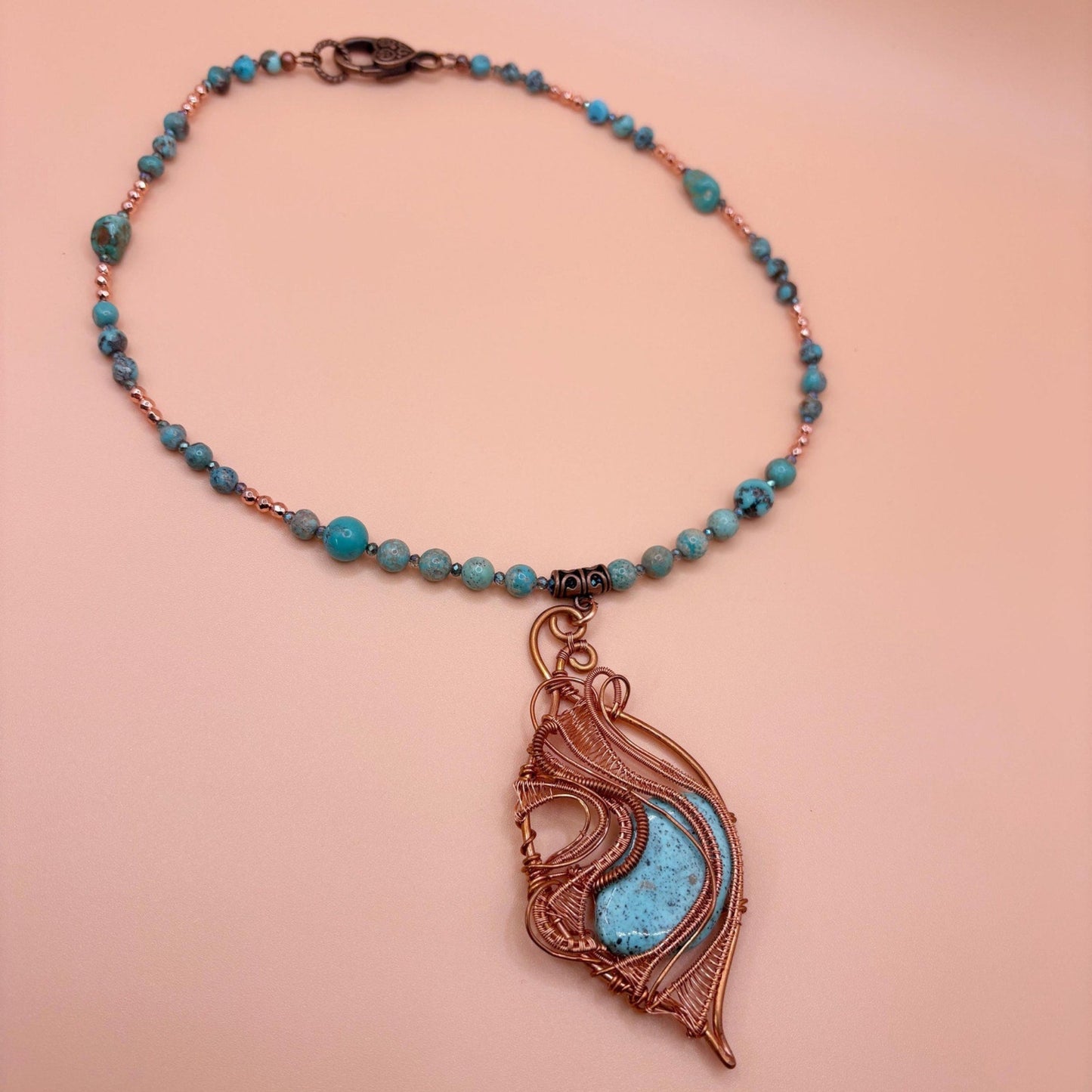 Necklace with turquoise beads and a copper pendant on a peach background