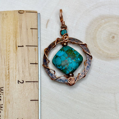Turquoise pendant with copper frame on a wooden surface with ruler for scale