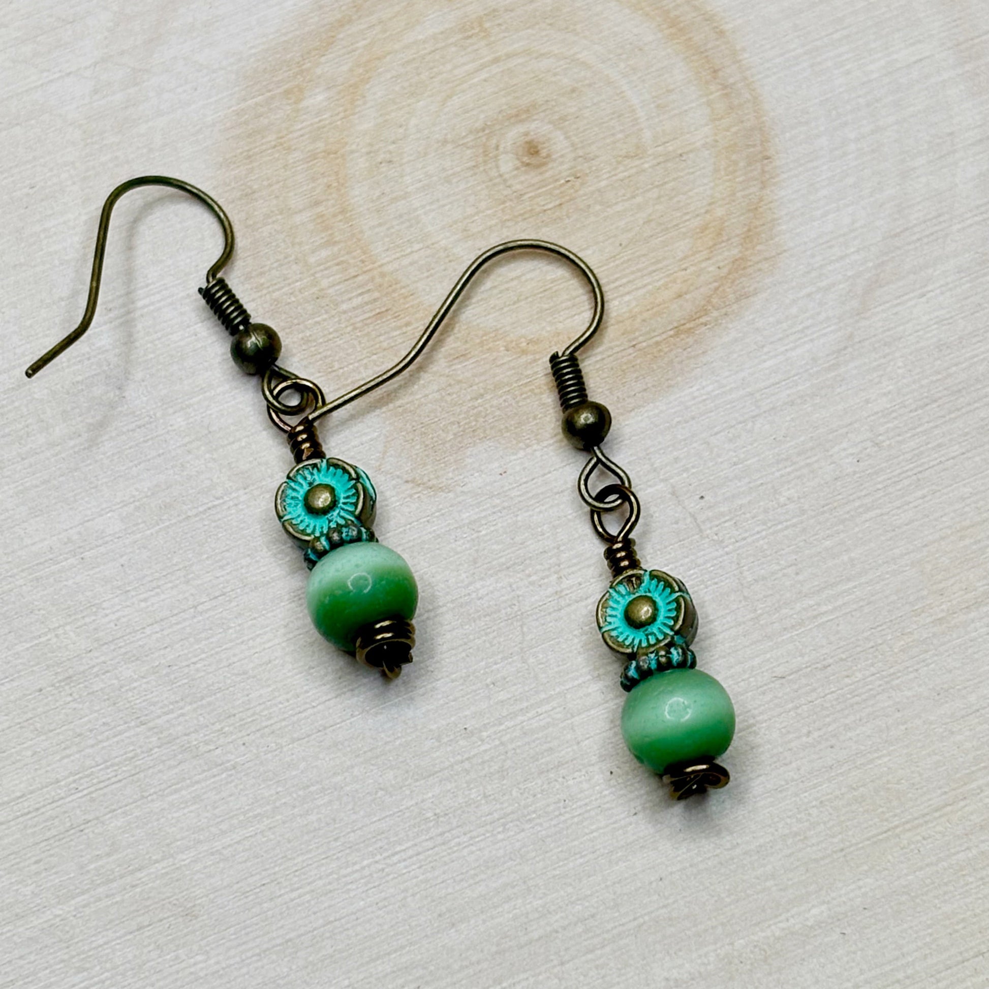 Pair of earrings with green beads and bronze accents on a wooden surface
