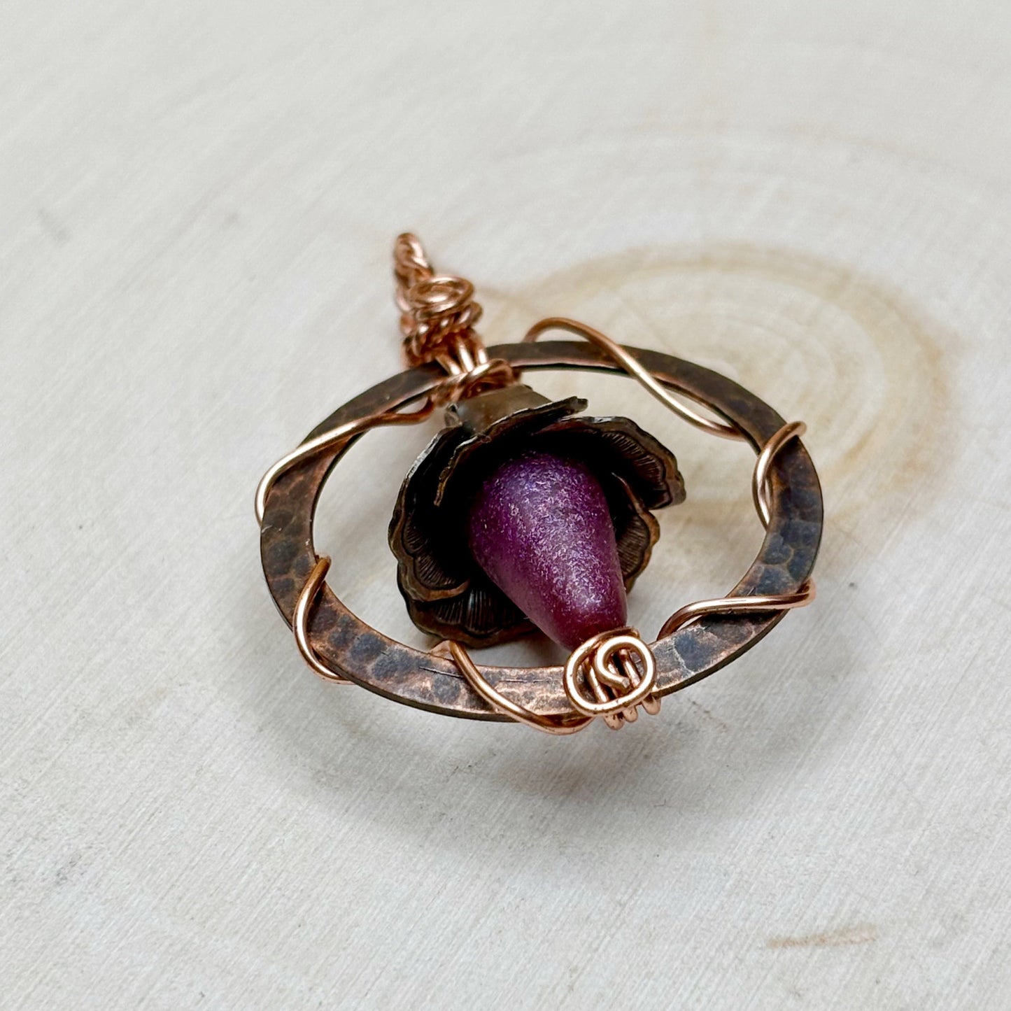 Rose-shaped pendant with purple center and copper wirework on a light background