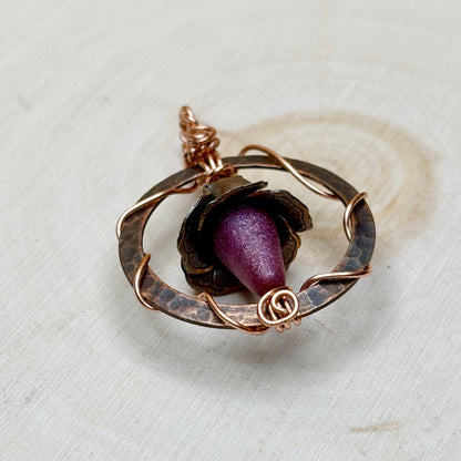 Rose-shaped pendant with purple center and copper wirework on a light background