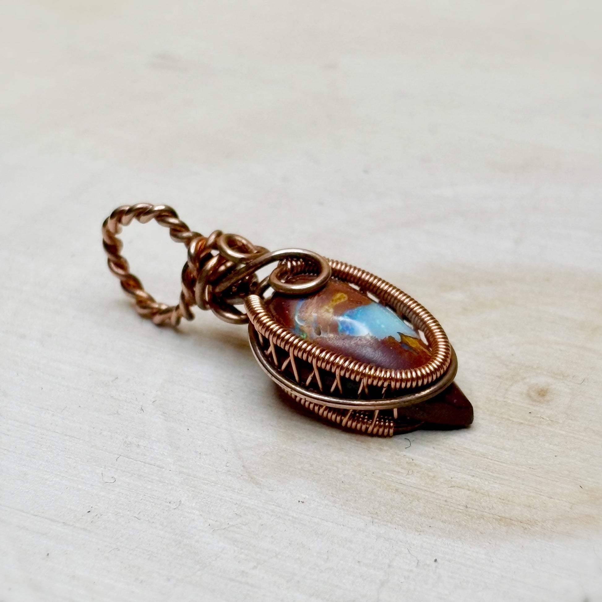 opal wire wrap pendant in copper with rainbow color in brown matrix on a wooden background