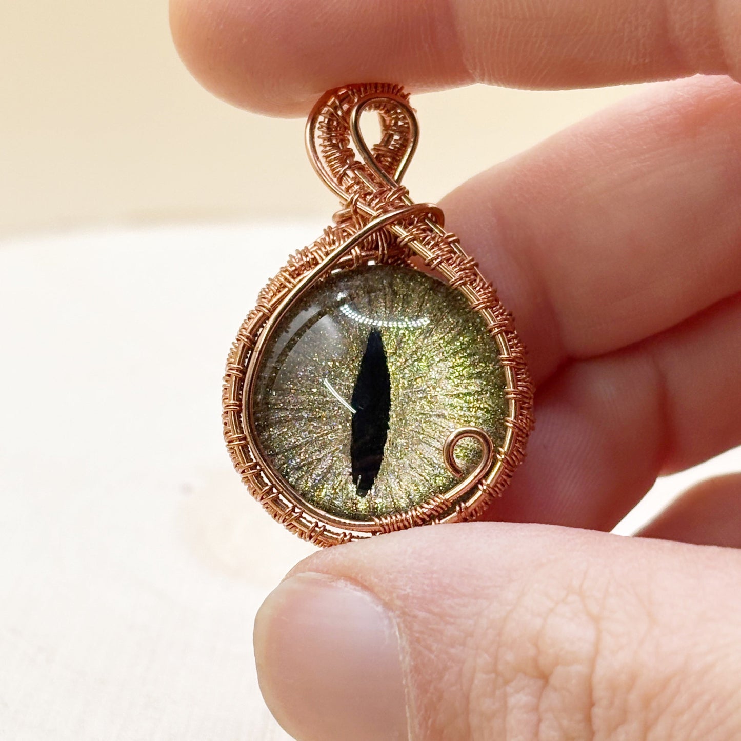 Hand holding a copper-wrapped pendant with a detailed eye design.