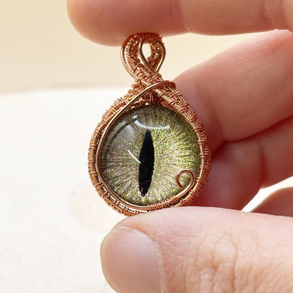 Hand holding a copper-wrapped pendant with a detailed eye design.