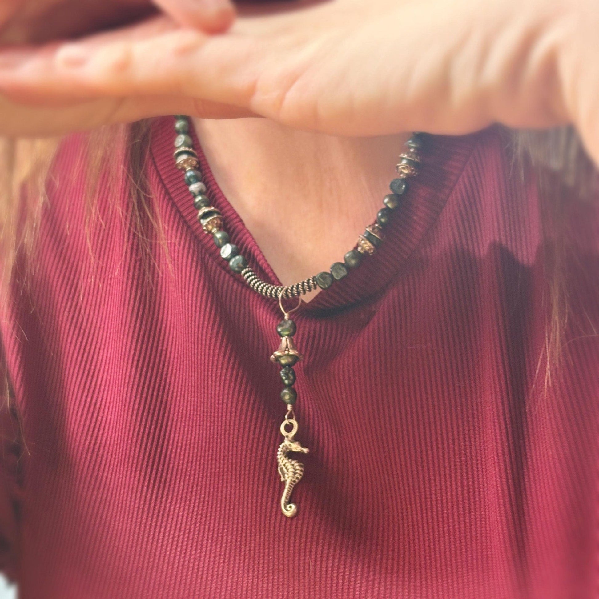 Person wearing a necklace with a seahorse pendant, blurred background