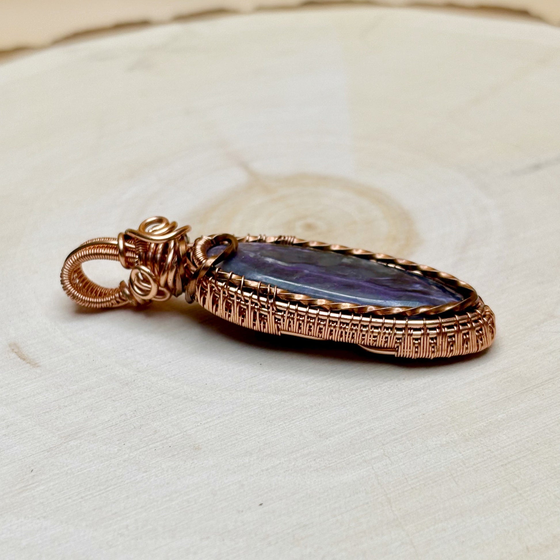 copper necklace pendant with purple stone on a textured beige surface