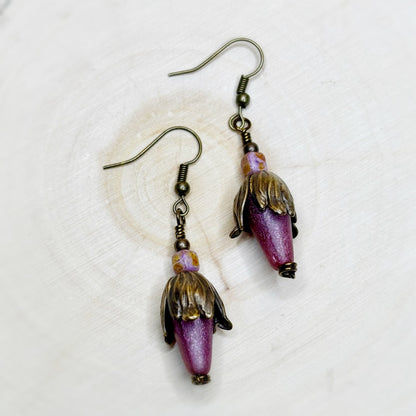 Pair of earrings with purple and gold beads on a white background