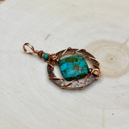Turquoise stone pendant with copper wirework on a light wooden surface