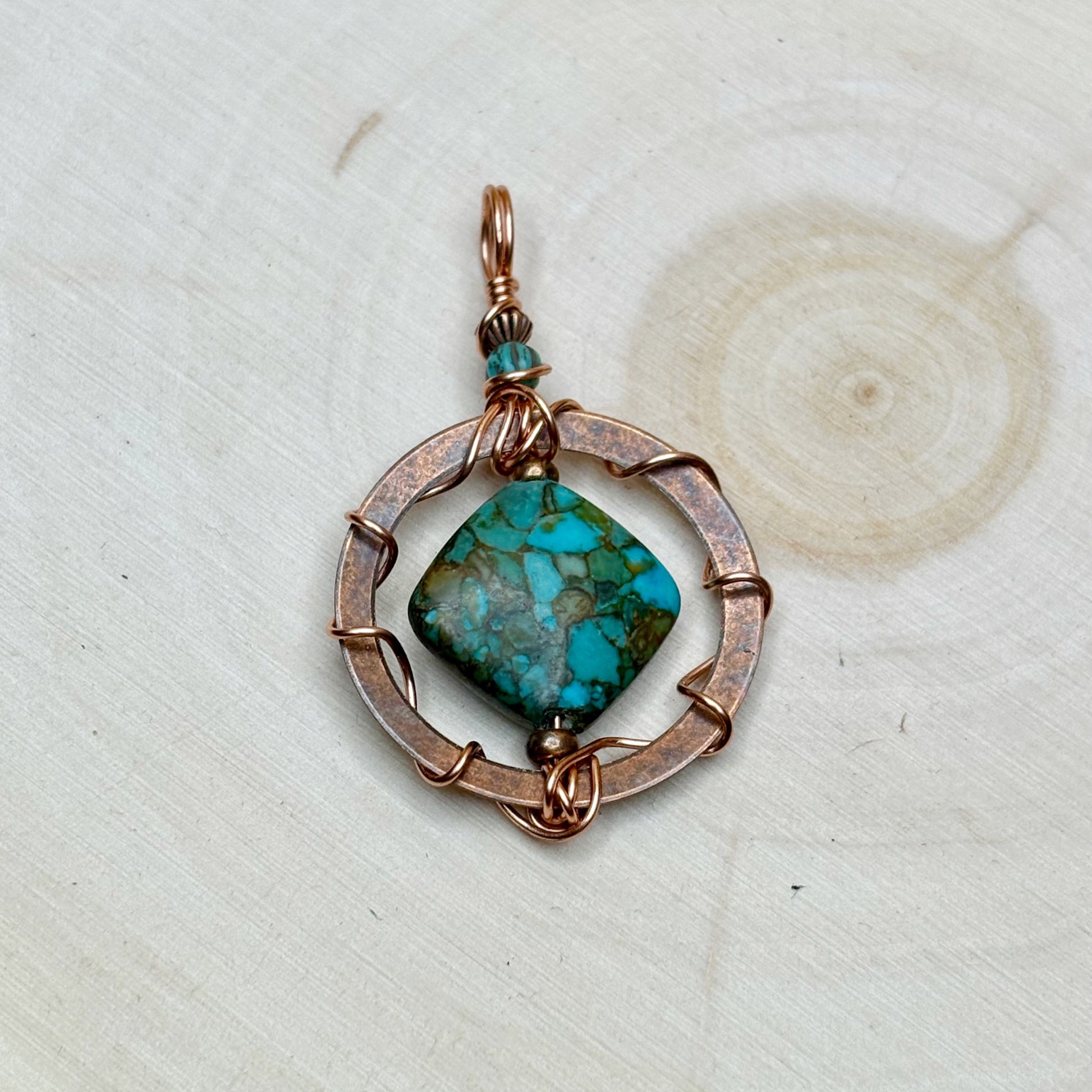Turquoise stone pendant with copper wire wrapping on a textured white background
