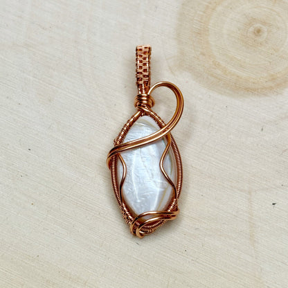 Copper-wrapped pendant with a white shell on a beige background