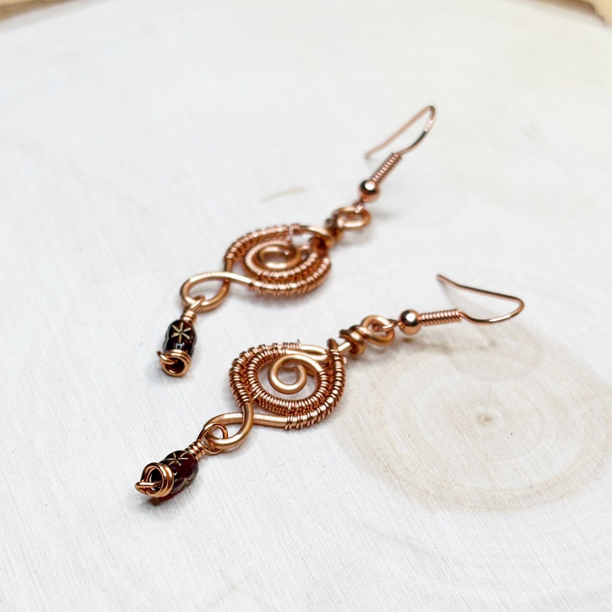 Pair of copper wire-wrapped earrings on a white wooden background