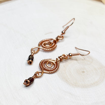 Pair of copper wire-wrapped earrings on a white wooden background