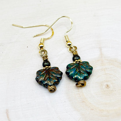 Pair of earrings with leaf-shaped beads on a light wooden surface