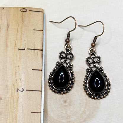 Pair of black teardrop earrings with bronze detailing on a wooden surface with a ruler for scale.
