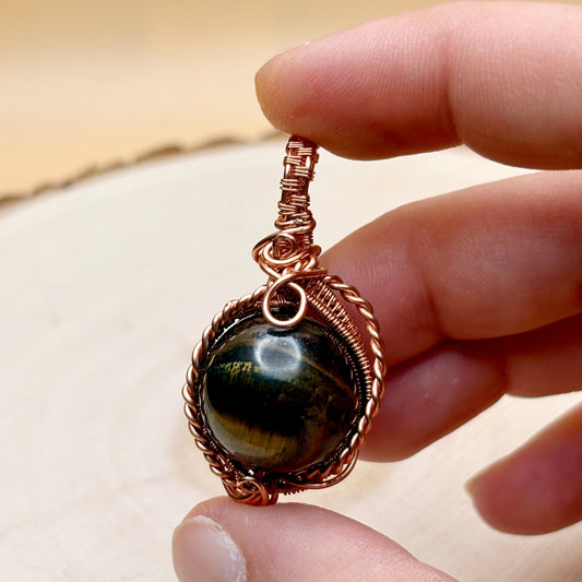Hand holding a copper-wrapped pendant with a black stone against a neutral background