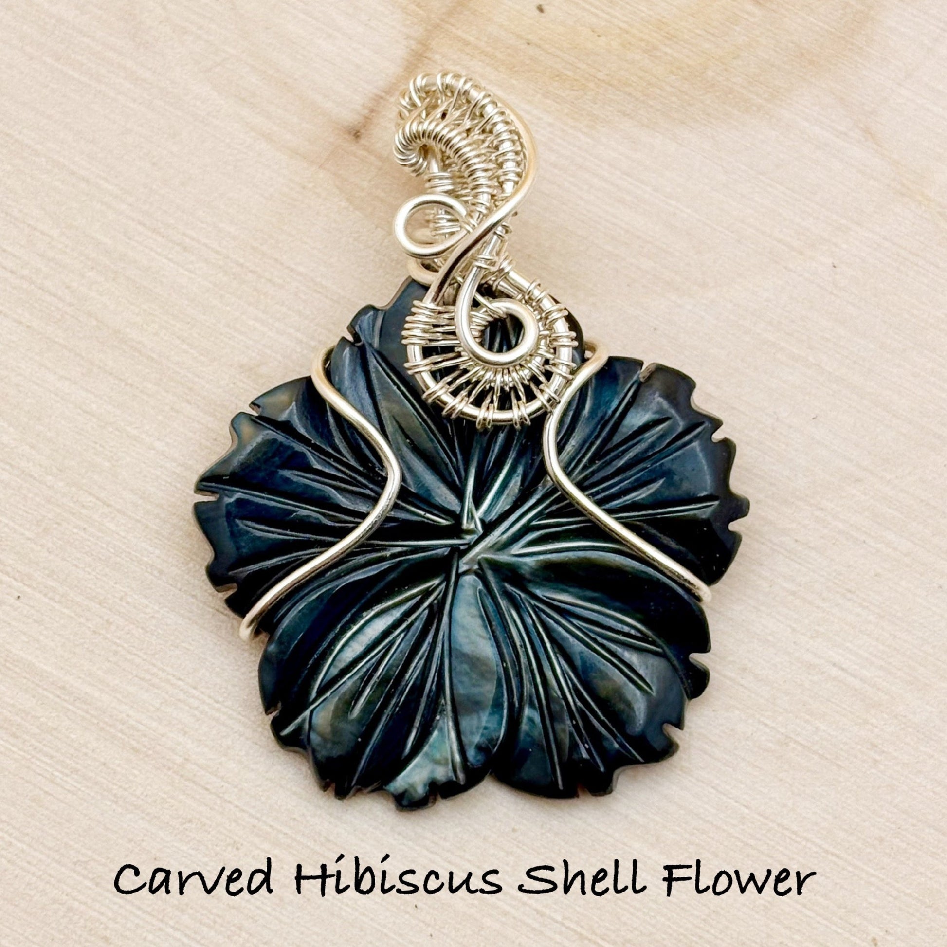 Carved Hibiscus Shell Flower pendant with silver wire wrapping on a beige background
