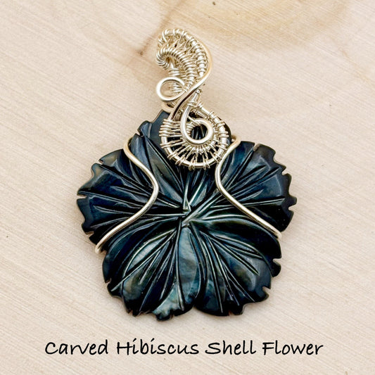 Carved Hibiscus Shell Flower pendant with silver wire wrapping on a beige background