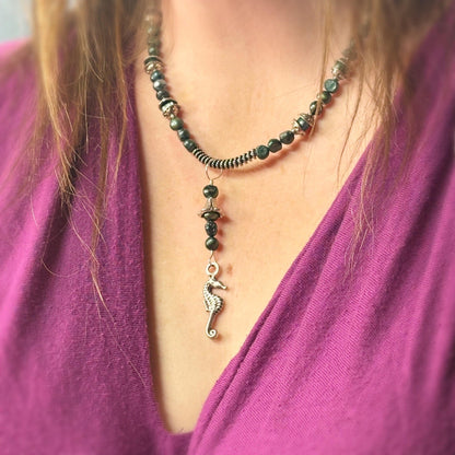 Necklace with a seahorse pendant worn by a person in a purple top