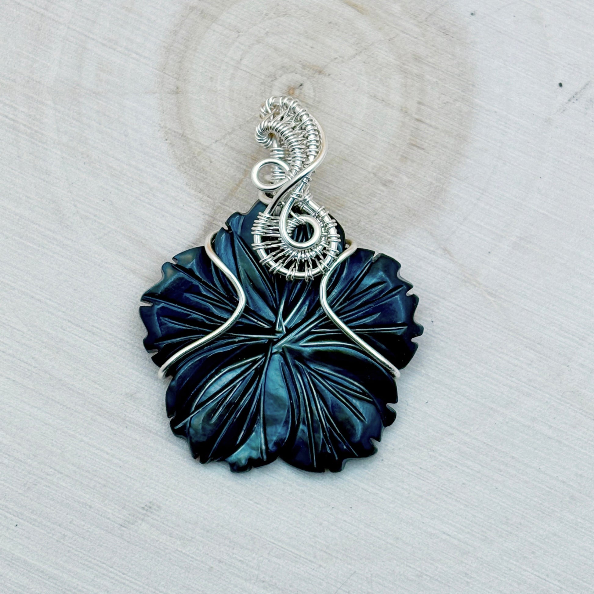 Blue flower shaped pendant with silver wire wrapping on a light background