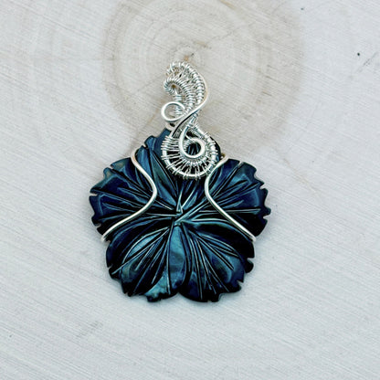 Blue flower shaped pendant with silver wire wrapping on a light background