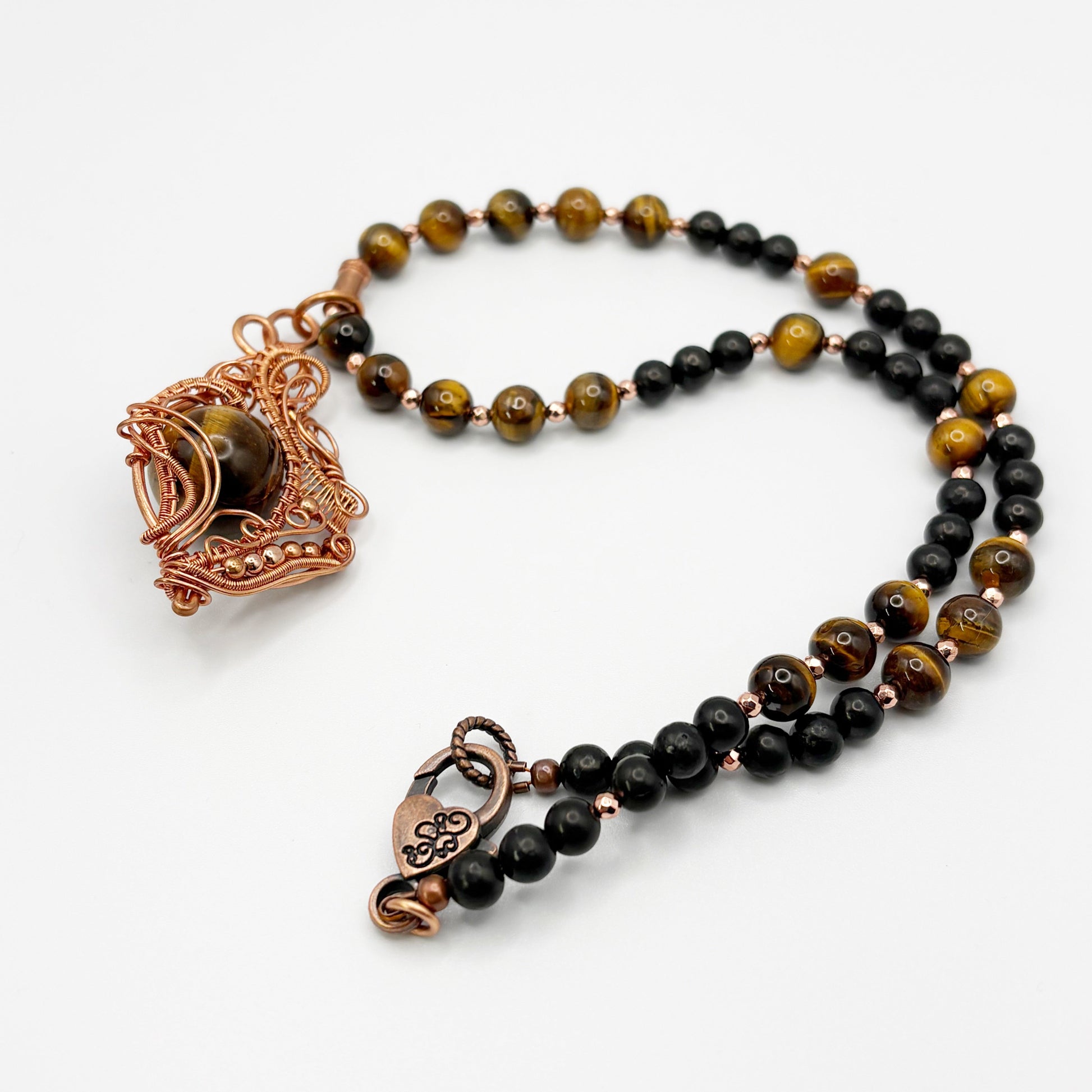 Necklace with black and brown beads and copper clasp on a white background