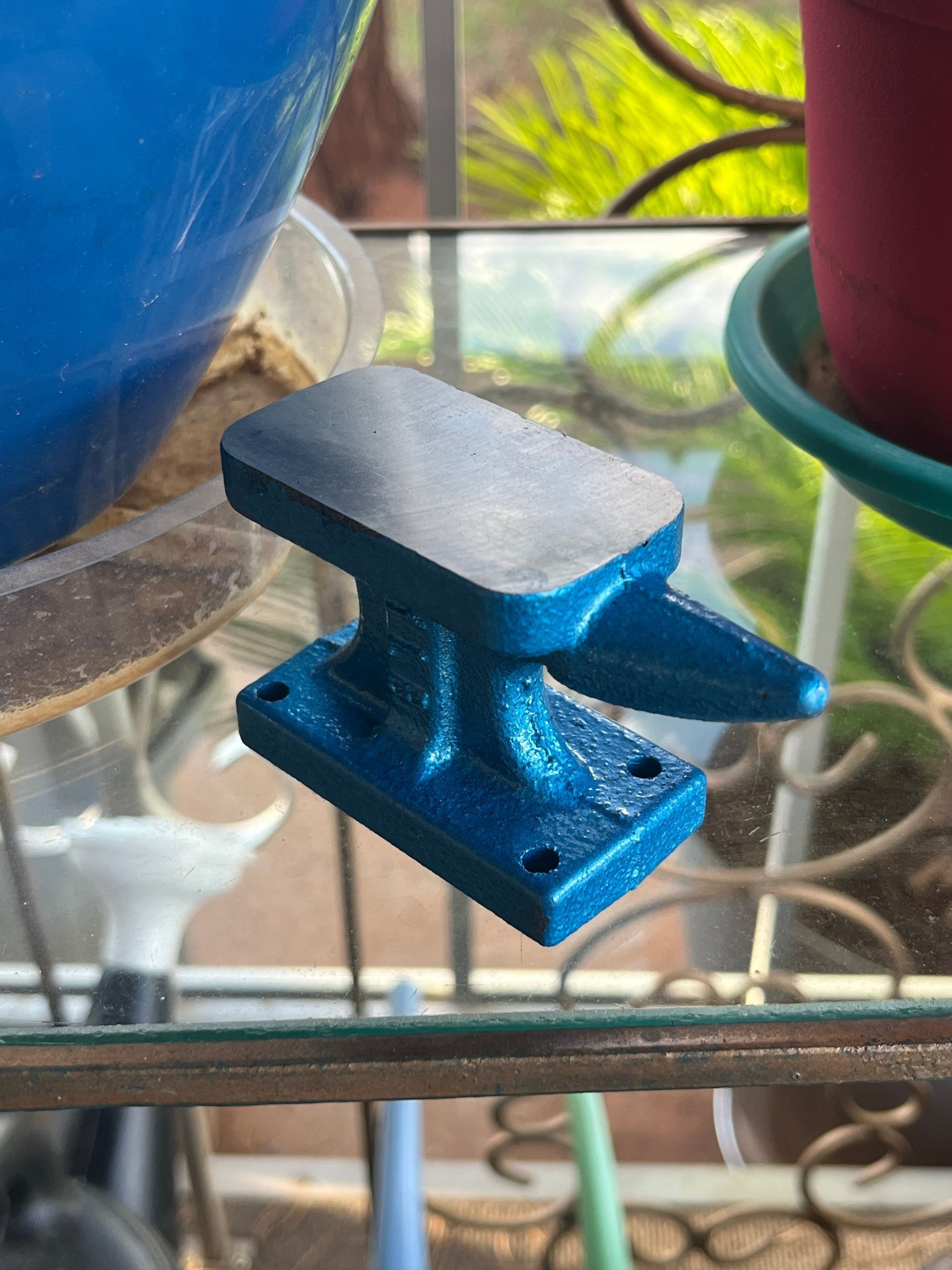 Blue anvil-shaped object on a glass surface with blurred outdoor background