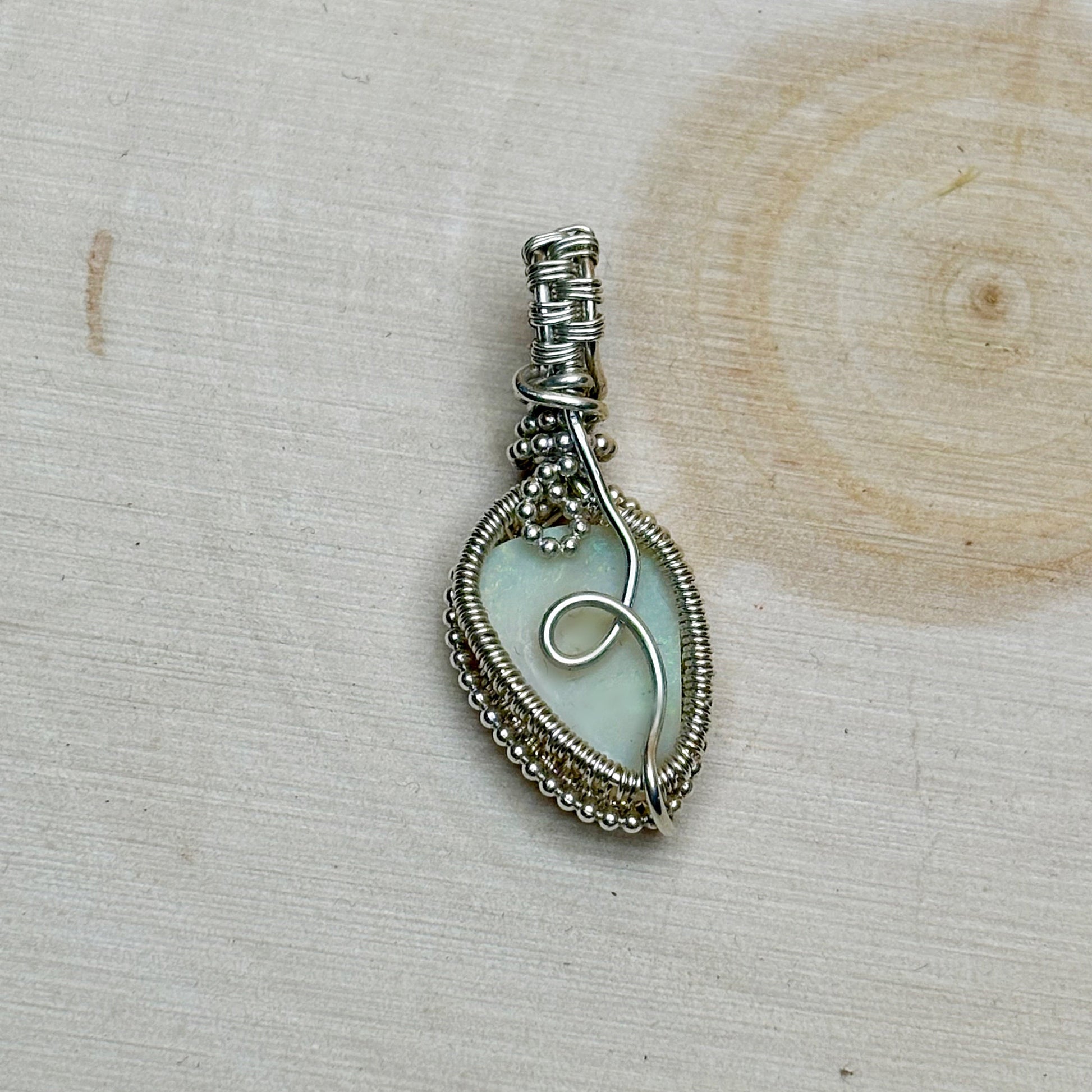 Silver wire-wrapped pendant with an opal center on a wooden surface