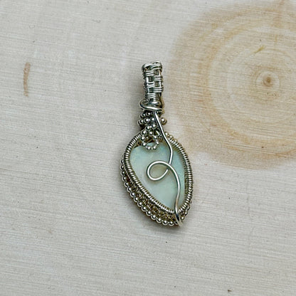 Silver wire-wrapped pendant with an opal center on a wooden surface