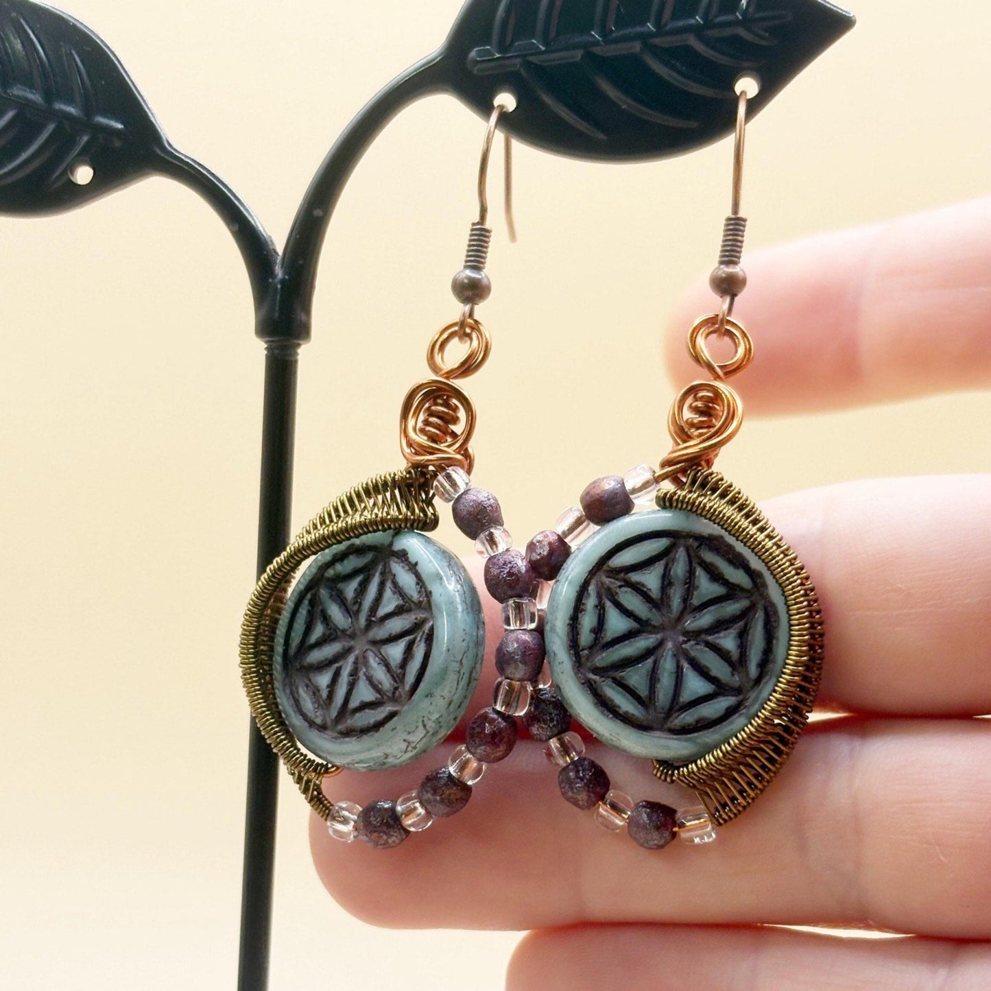 Pair of earrings with decorative glass beads held by a hand against a neutral background