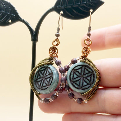 Pair of earrings with decorative glass beads held by a hand against a neutral background