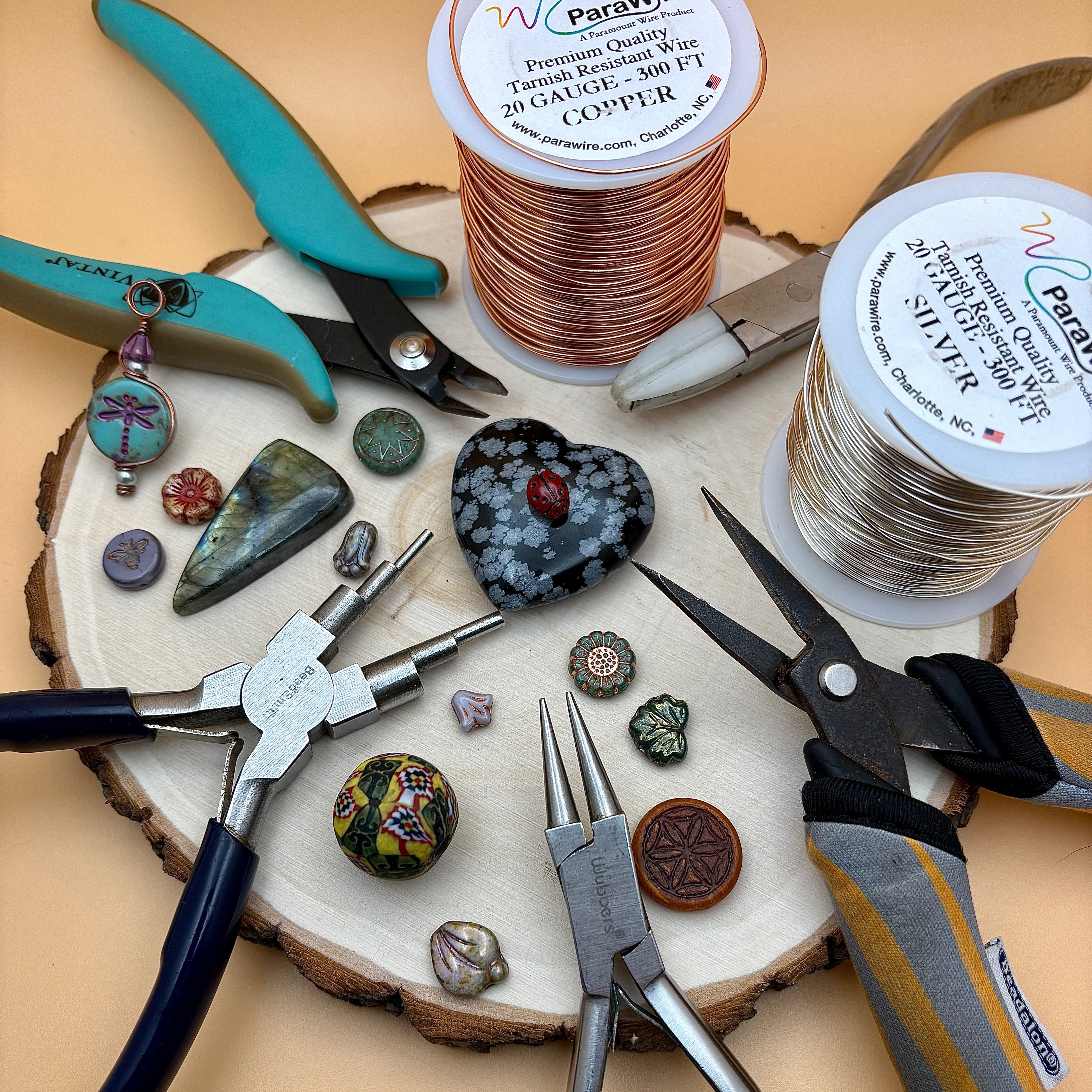 Jewelry-making tools and materials on a wooden surface with spools of wire and gemstones.