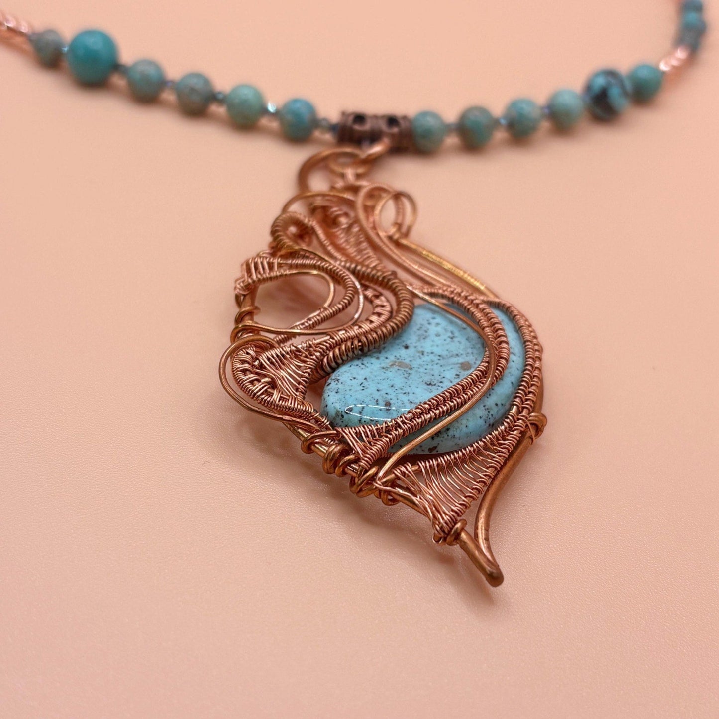 Necklace with a turquoise stone and copper wire-wrapped pendant on a beige background